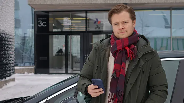 Mies seisomassa mustan auton edessä talvisäässä puhelin kädessä